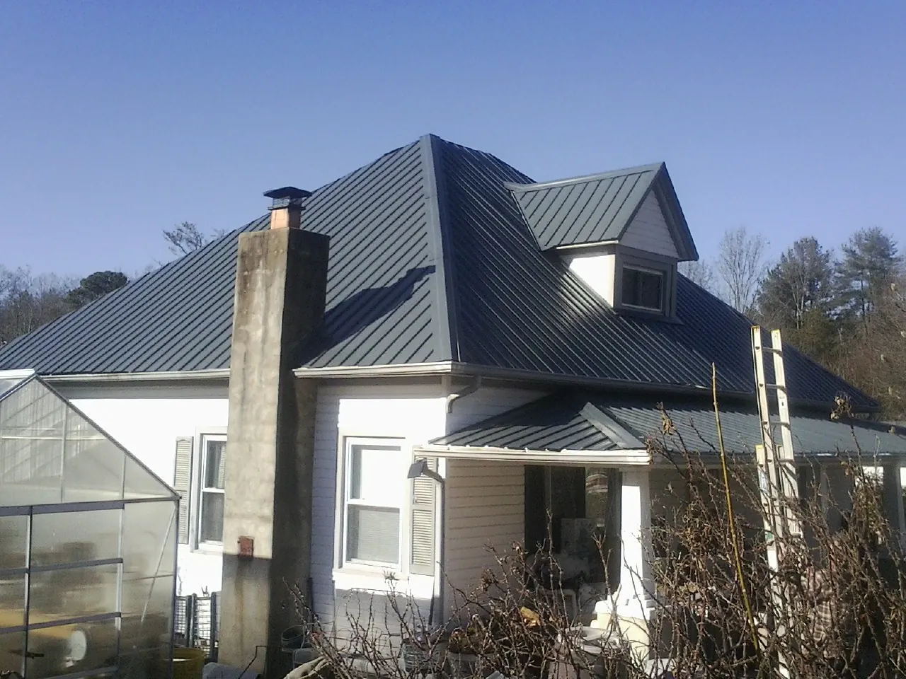 Dark blue standing seam metal roof on a white farmhouse with dormer — Slate & Tile Roof Repair by Roofing Brothers in Broken Arrow