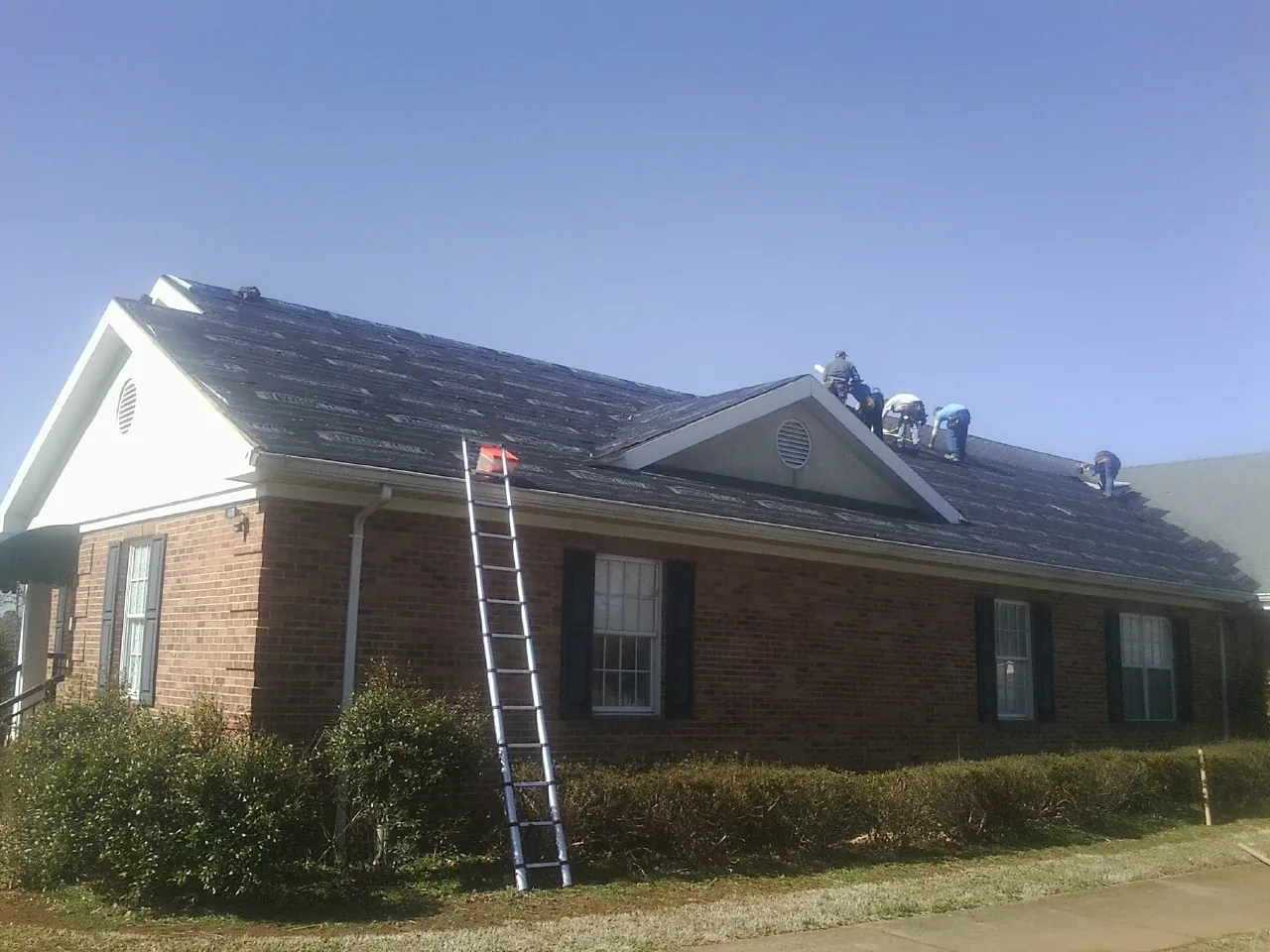Crew tearing shingles off a brick ranch roof with a ladder set — Metal Roof Repair work by our crew in Broken Arrow