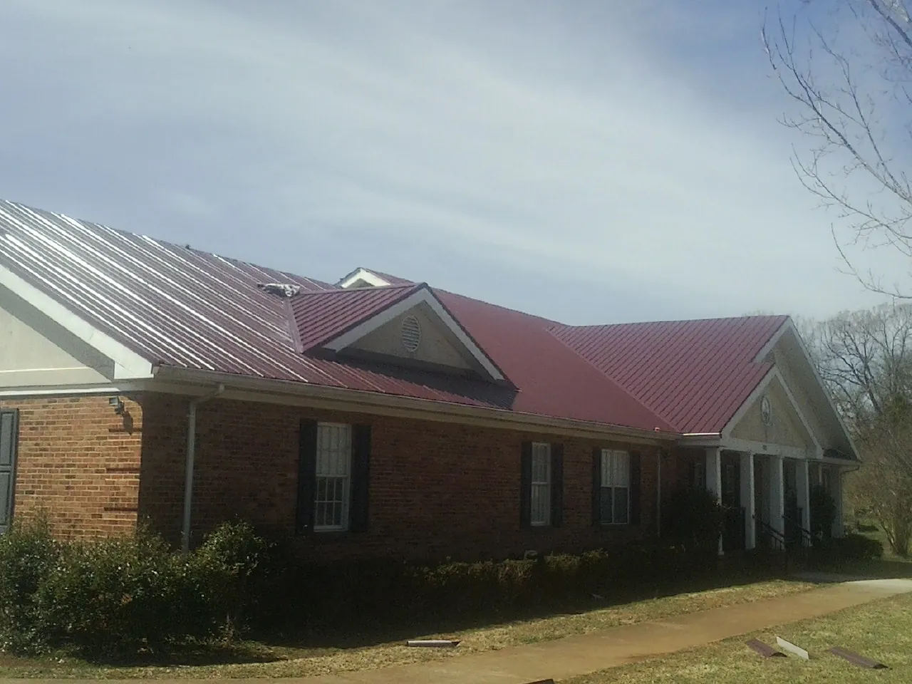 Red metal roof with gabled entries on a long brick building, from a Hail Damage Roof Repair job in Broken Arrow