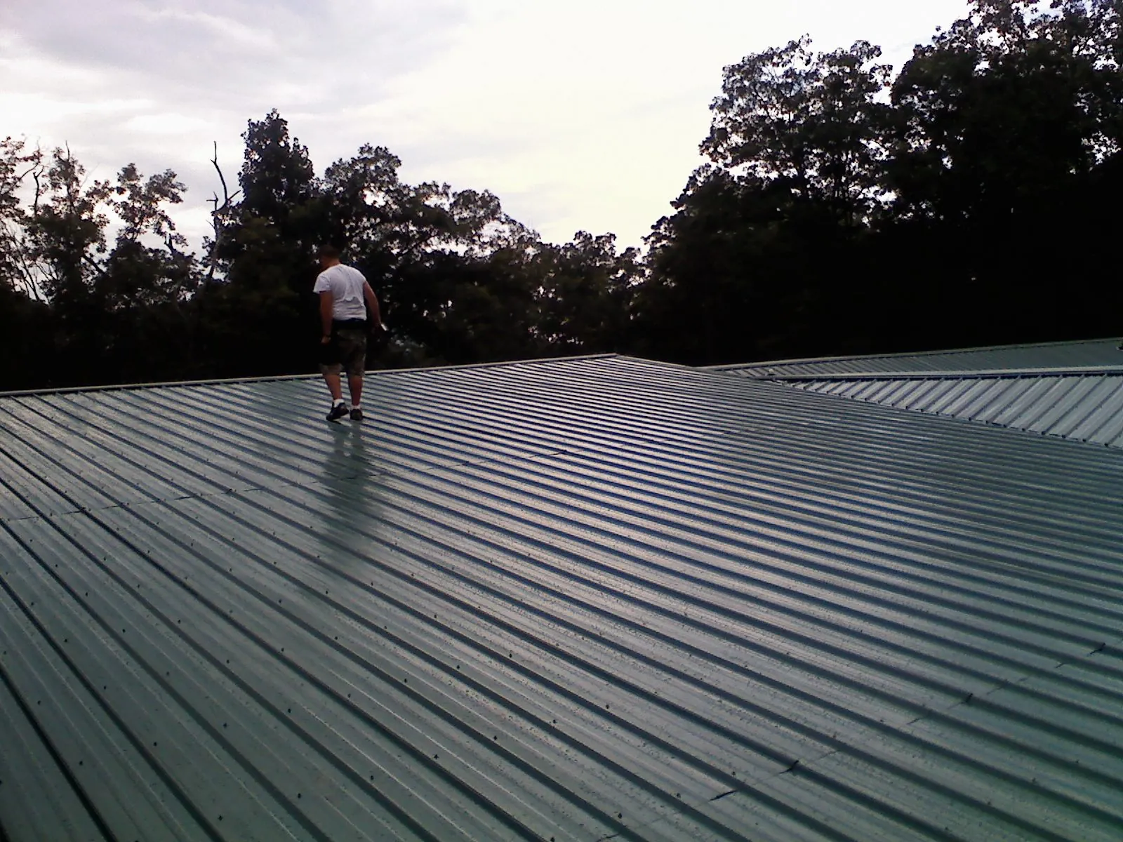 Roofer walking a wide expanse of new green metal roofing in Broken Arrow
