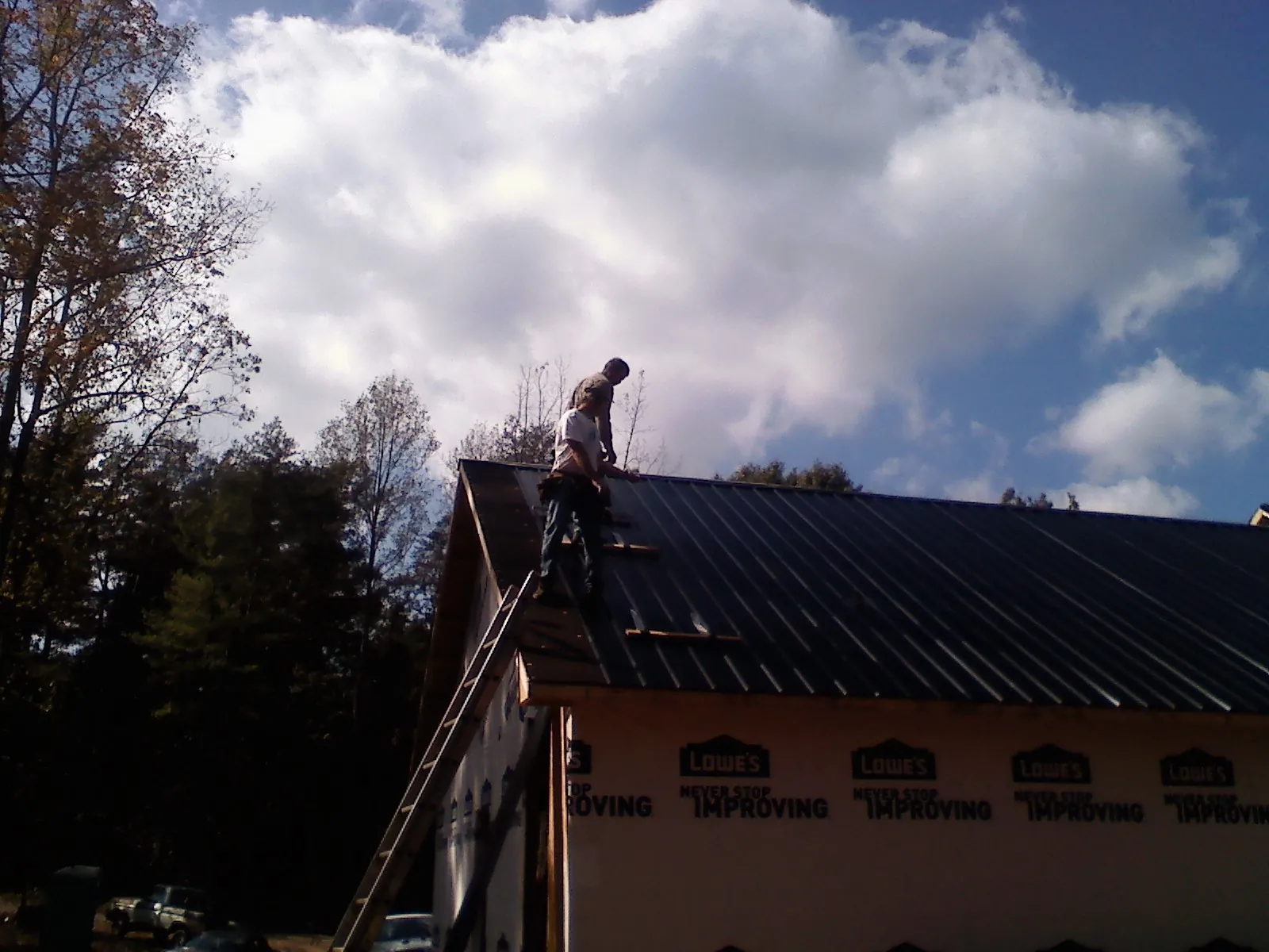 Roofer fastening dark metal panels high against a cloudy sky, from a Roof Inspection job in Broken Arrow