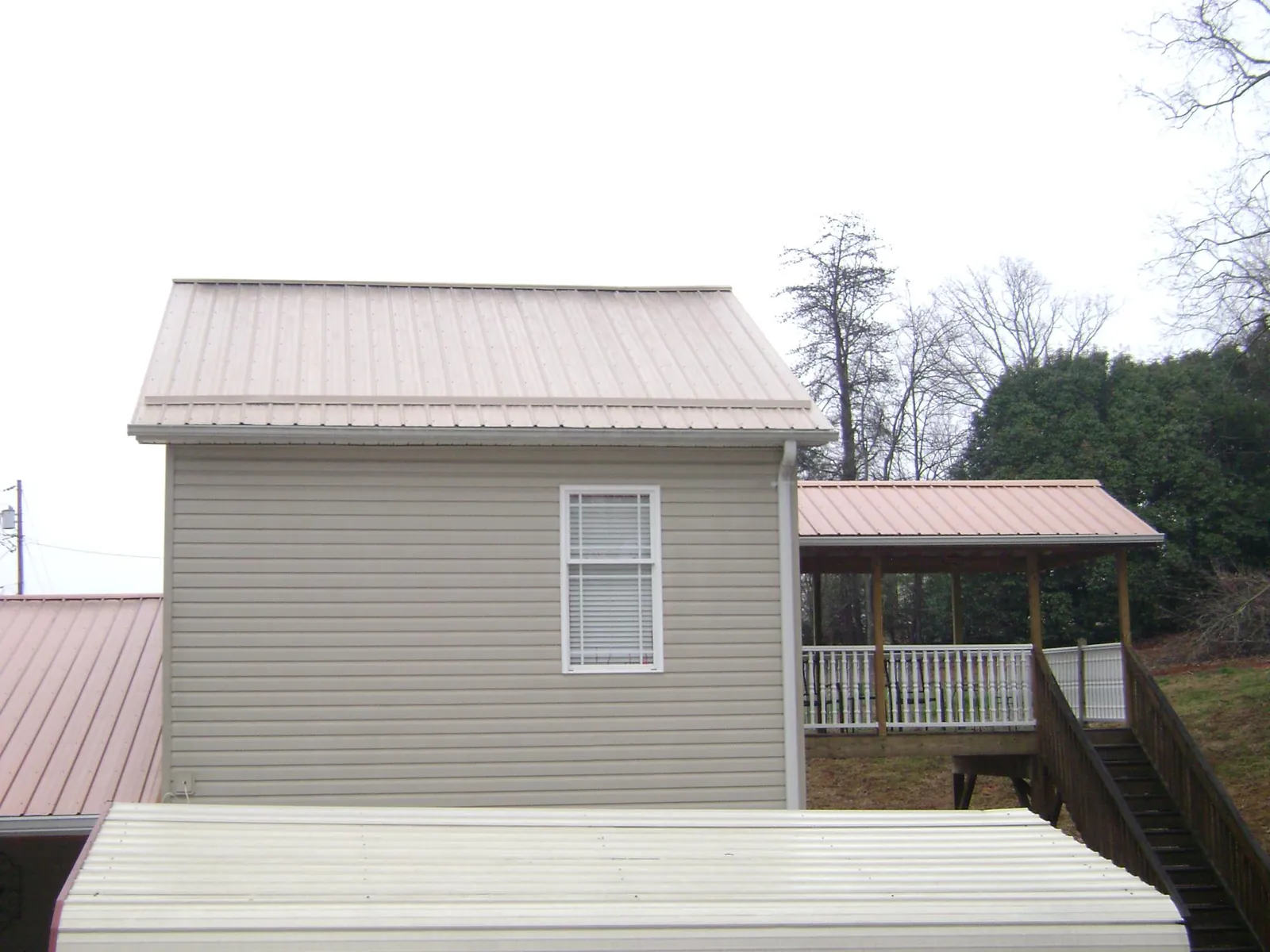 Tan metal roofs on a two story addition and attached porch, from a Roof Replacement job in Broken Arrow