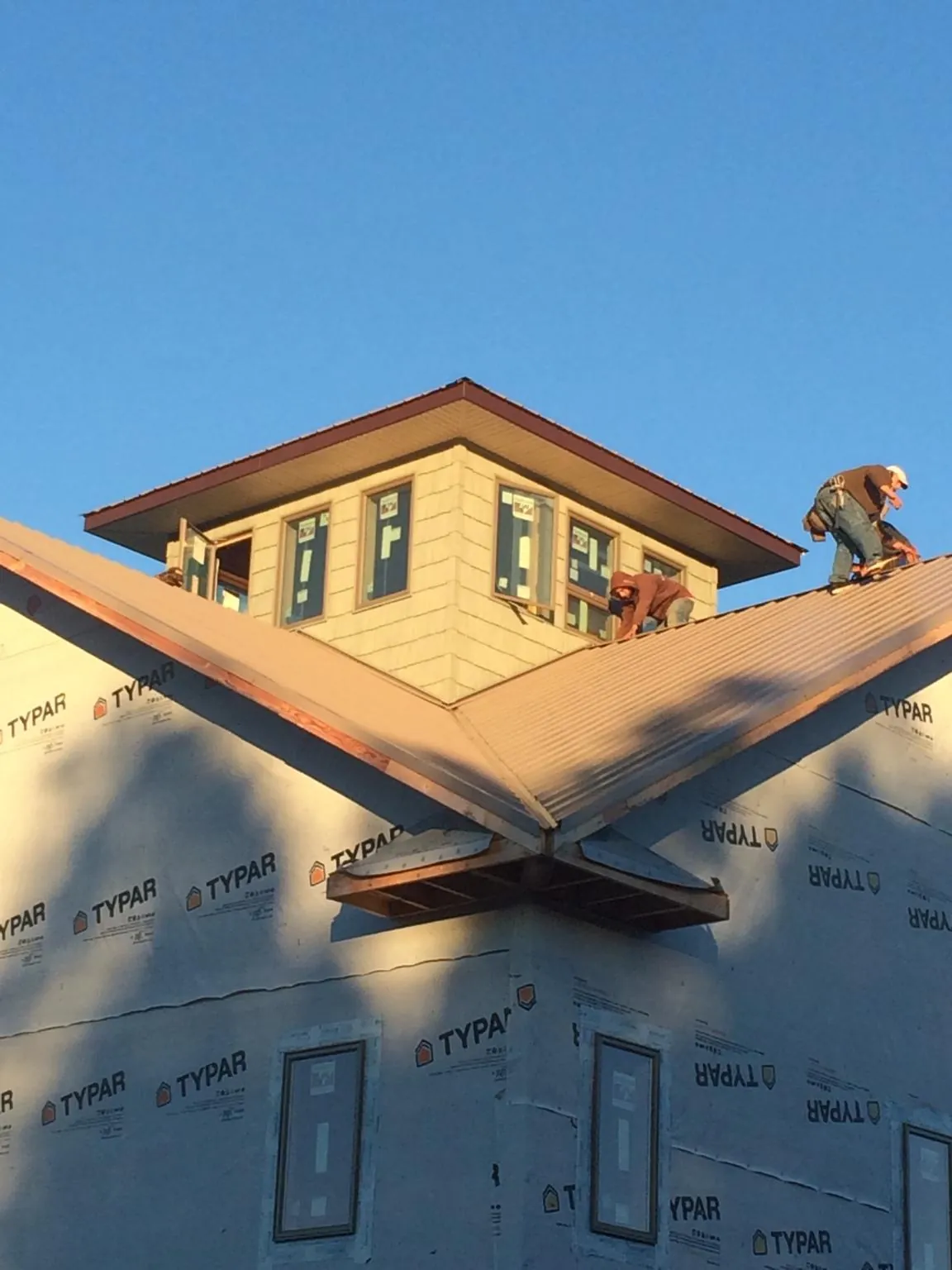 Roofers working around a rooftop cupola on a new metal roof at sunset — Roof Waterproofing in Broken Arrow by Roofing Brothers